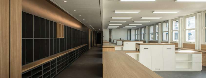 Vue en enfilade entre mur de casiers et plateau de bureaux éclairé, SAV Horlogerie Chanel ; conception lumière Ponctuelle