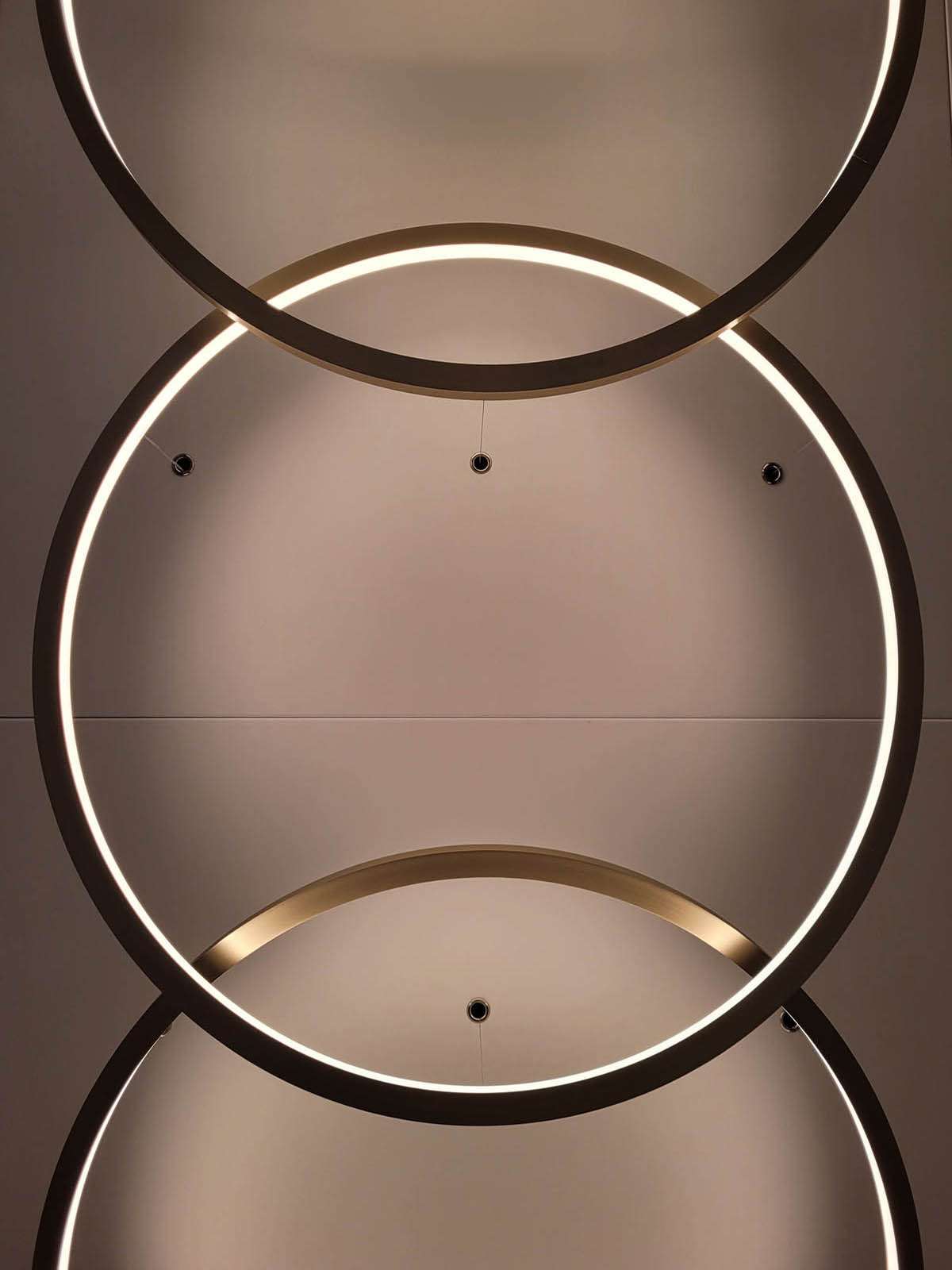 Détail de luminaires circulaires entrelacés au plafond, conception lumière bureaux Paris Ponctuelle