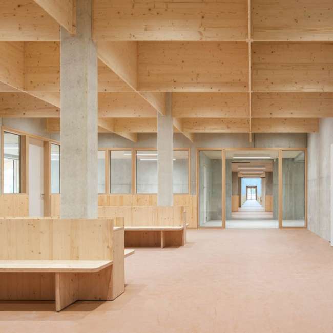 Espace commun sous charpente bois lamellé-collé avec bancs intégrés, conception lumière Ponctuelle