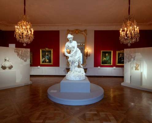Salon rouge avec lustres à bougies et sculpture en marbre, exposition Trésors retrouvés au Château de Versailles, conception lumière Ponctuelle