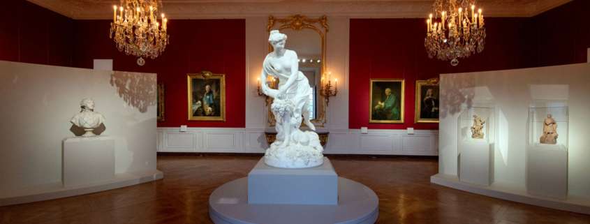 Salon rouge avec lustres à bougies et sculpture en marbre, exposition Trésors retrouvés au Château de Versailles, conception lumière Ponctuelle