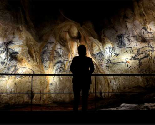 Visiteur en silhouette face aux fresques rupestres éclairées de la reconstitution de la grotte Chauvet, conception lumière Ponctuelle