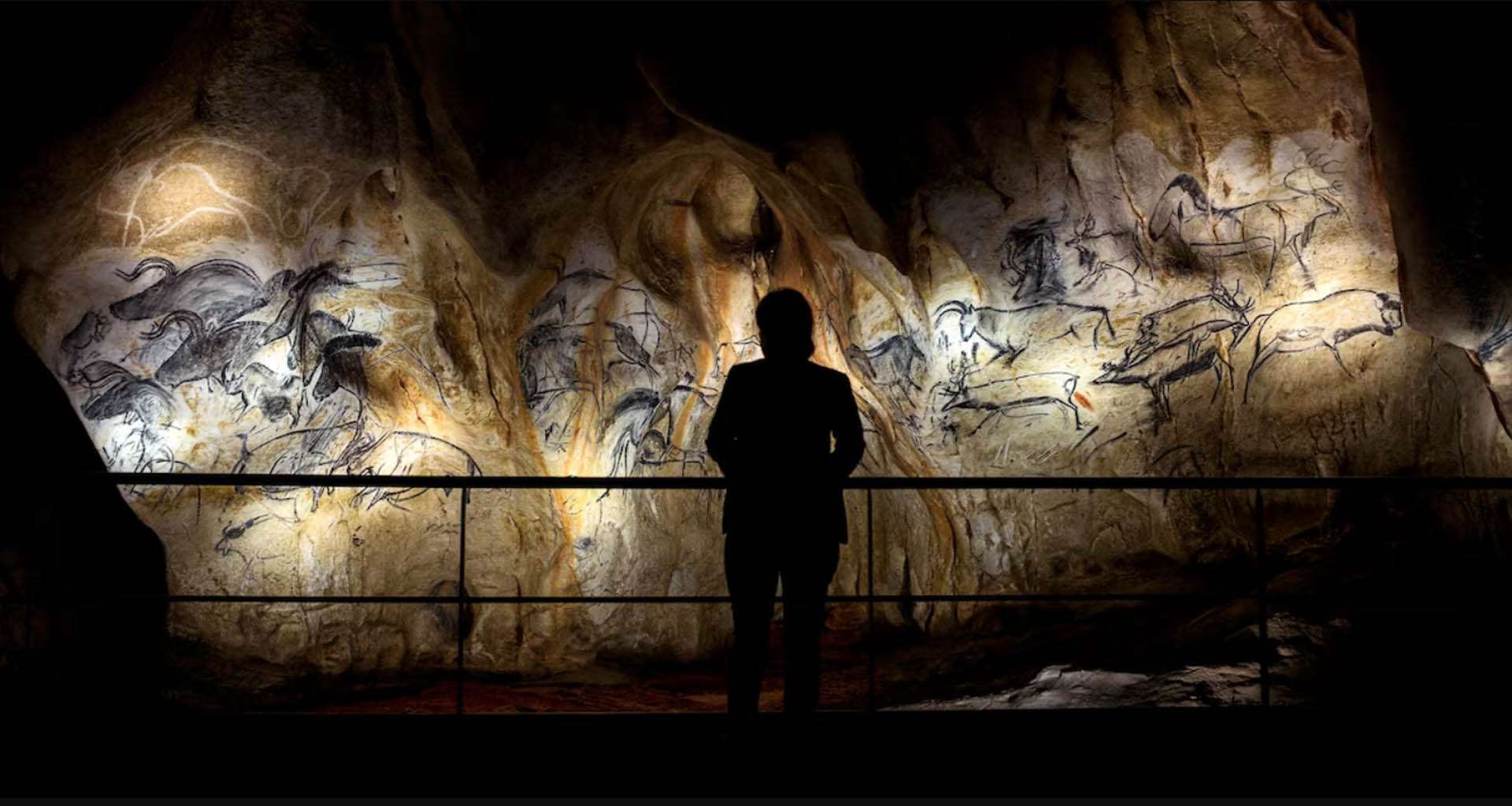 Visiteur en silhouette face aux fresques rupestres éclairées de la reconstitution de la grotte Chauvet, conception lumière Ponctuelle