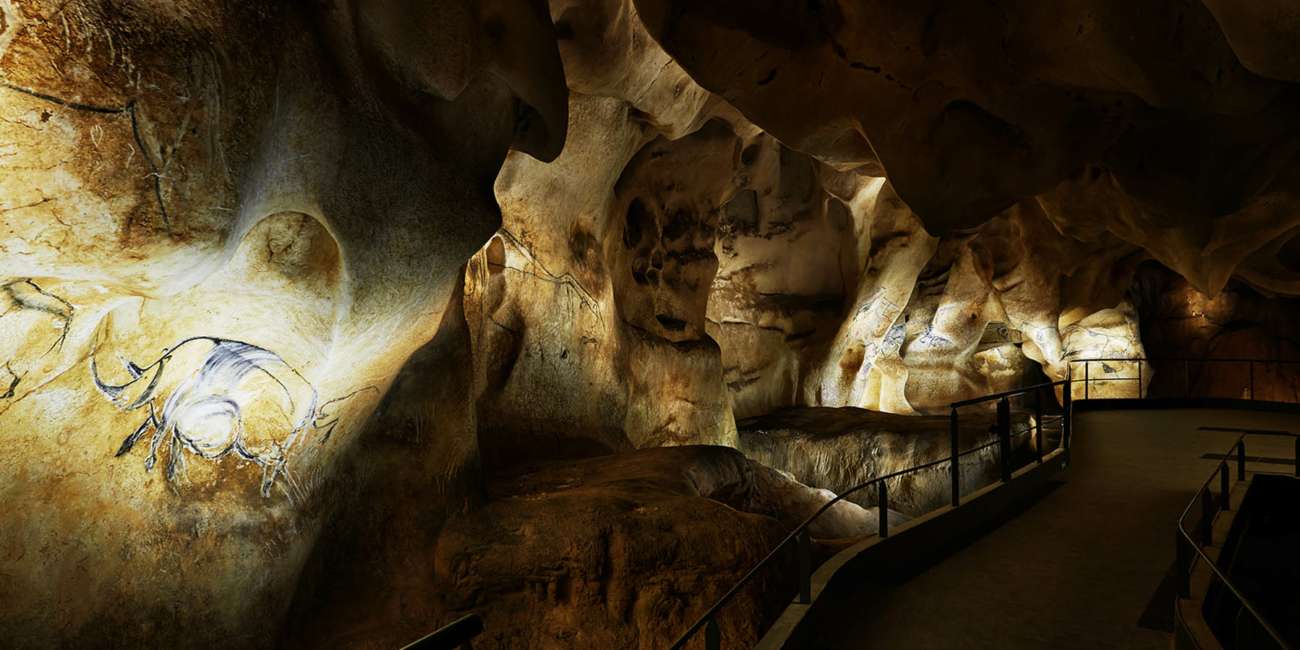 Fresque de bison éclairée et parcours de visite courbe dans la reconstitution de la grotte Chauvet, conception lumière Ponctuelle