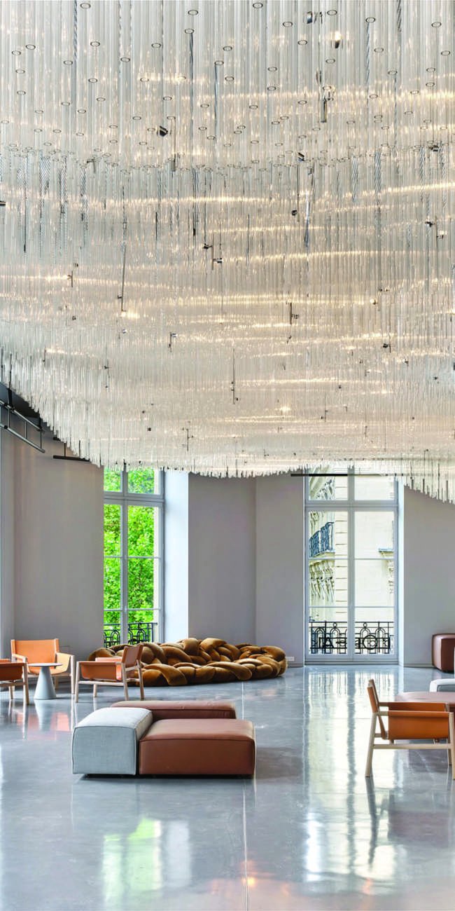 Hall d'accueil sous un lustre monumental en tubes de verre suspendus, mise en lumière L'Oréal Le Visionnaire