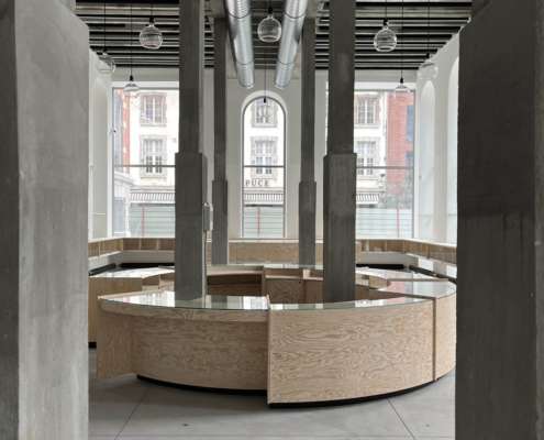 Hall du Smart Center de Tournai avec comptoir circulaire en bois et suspensions en verre, conception lumière Ponctuelle