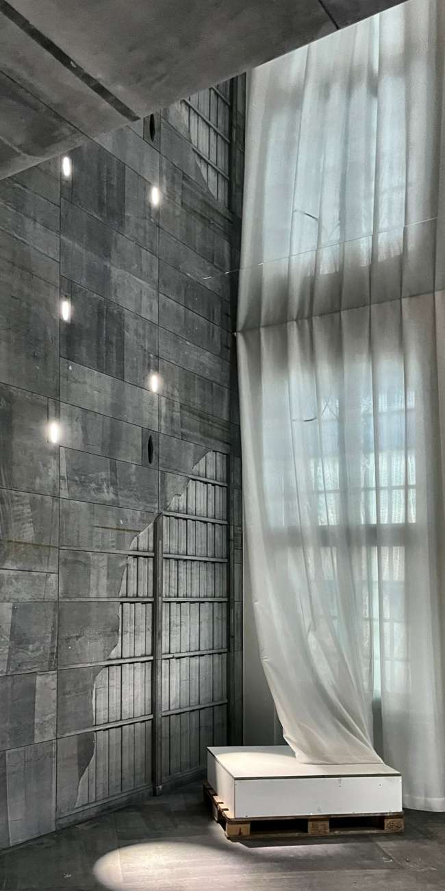 Conception lumière Smart Center à Tournai : mur en béton brut ponctué d'encastrés et voilage blanc éclairé en lumière naturelle