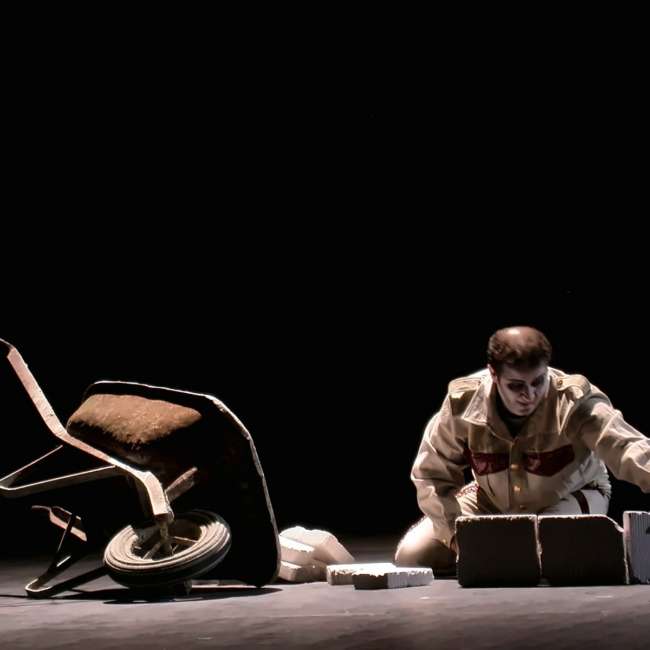 Personnage agenouillé près de briques et d'une brouette renversée, éclairage latéral sur fond noir, Wozzeck, Opéra de Nantes, conception lumière Ponctuelle